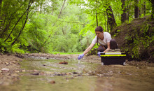 Woman Scientist Environmentalist Sitting Near The Creek. She Taking Sample Of Water