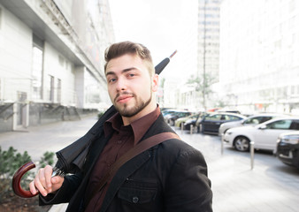 Man with a beard and an umbrella in his hands looks at the camera and smiles against the backdrop of the urban landscape.Man with an umbrella in his hands walks around the city.