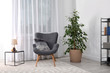 Stylish room interior with armchair and potted ficus