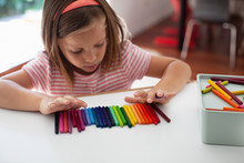 A Child Lines Up Colorful Crayons In A Row. 