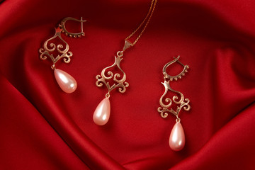 Beautiful precious women's jewelry, close-up. Pearl Golden Necklace and Earrings on red silk background with copy space