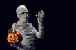 Studio shot portrait  of young man in costume  dressed as a halloween  cosplay of scary mummy pose like a hold jack'o pumpkin clamber acting on isolated black background.