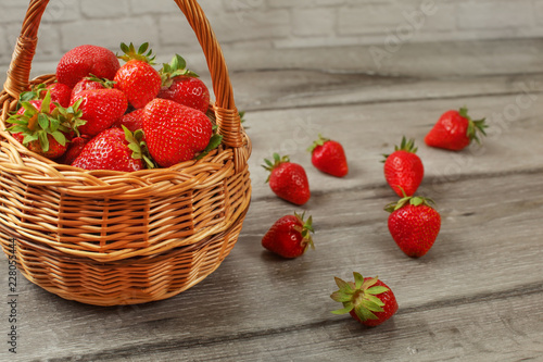 Fotografering Basket with strawberries, some of them spilled on gray wood desk.