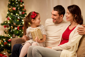 holidays, family and celebration concept - happy mother, father and little daughter with christmas present at home