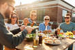 © Syda Productions - leisure and people concept - happy friends eating and drinking at barbecue party on rooftop