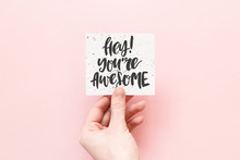 Minimal Composition On A Pink Pastel Background With Girl's Hand Hold Card With Quote - Hey! You're Awesome