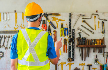 Portrait of a male construction worker in the helmet choosing the many different rusty old tools hanging on a wall