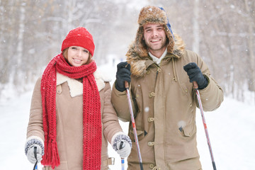 Wall Mural - Waist up portrait of active young couple skiing in snowy winter forest on date
 and smiling at camera