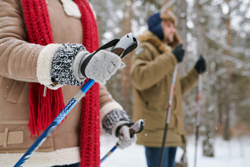 Wall Mural - Side view portrait of active young couple enjoying skiing in beautiful winter forest, focus on unrecognizable woman holding ski poles, copy space