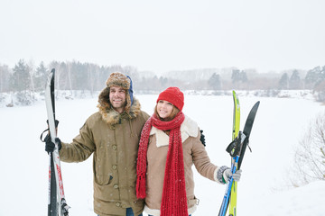 Wall Mural - Waist up portrait of loving young couple embracing and smiling happily while taking break during skiing trip and posing against beautiful winter landscape, copy space