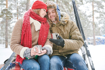 Wall Mural - Portrait of loving young couple cuddling tenderly and  enjoying hot cocoa during date in beautiful winter forest, copy space