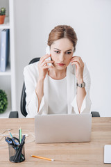 stressed businesswoman talking on smartphone at workplace with laptop