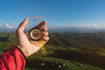 Man searching direction with a compass in his hand in the summer mountains point of view. Direction Search