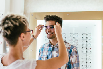 Wall Mural - Attractive young couple in optical store buying glasses and smiling