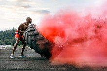 Handsome African American Muscular Man Flipping Burning Big Tire Outdoor With Smoke