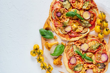 Veggie pizza with wild mushrooms,  vegetables and spices on the concrete background. Vegetarian pizza decorated with fresh yellow cherry tomatoes on the white kitchen table. Top view with copy space