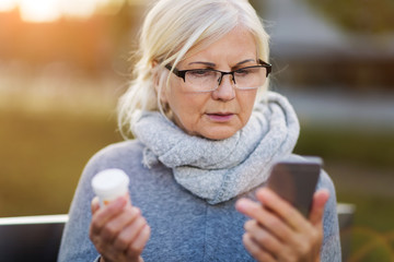 Woman holding smartphone and pill bottle