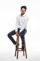 Wall Mural - Young Indian man sitting on chair and possing isolated for white background