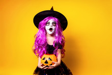 Small Girl In Halloween Witch Dress And Hat Scaring And Making Faces Isolated On Yellow Background. Trick Or Treat.