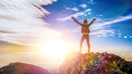 the girl stands on top of the mountain and enjoys the view of the valley. at the dawn, hands up