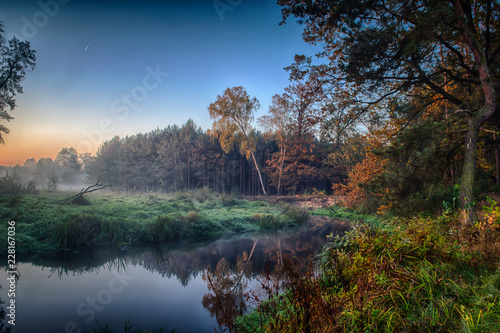 Rzeka we mgle, tuż przed wschodem słońca. Ciepły blask w chmurach od pierwszy...