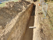 Open trench with small diameter water pipe and heap of ground