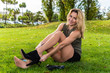 Beautiful young blond woman wearing tan pantyhose changing her heels behind a grassy knoll.