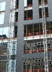 Wall Mural - close up view of a modern construction site with hoists running up the tall building with steel girders with black panels and windows being installed