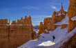 Photographer hiking on a snowy winter day in the orange canyon of Bryce National Park, Utah