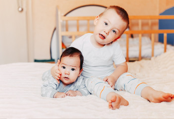 Cute little baby with elder brother lying on bed at home