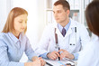 © rogerphoto - Two doctors  and  patient sitting at the table in medical cabinet.