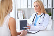 © rogerphoto - Doctor and patient discussing something while sitting at the table at hospital. Physician using tablet pc for information demonstration. Medicine and health care concept