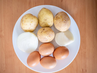 Top view of potatoes, eggs and onions in plate on wooden table.