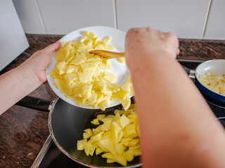 Hands throwing laminated potatoes from a white plate to black pan. Spanish omelet recipe.