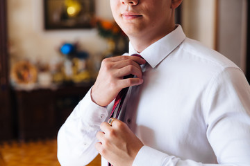 Wall Mural - Close-up of a cropped frame of a slender business man in a trendy suit wearing dark trousers and a white shirt is holding a tie in his hands. A businessman is going to try on a red tie.