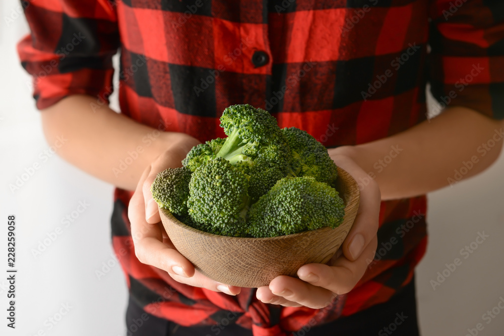 Woman holding bowl with fresh broccoli on light background, closeup