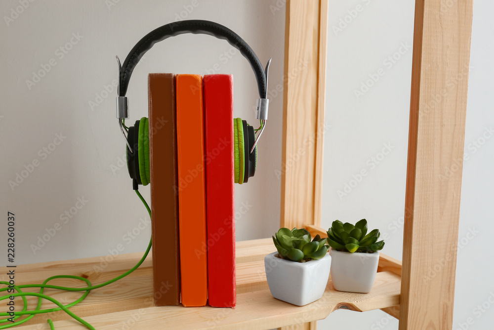 Modern headphones and books on wooden shelf. Concept of audiobook