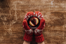 cropped image of woman in mittens holding glass of mulled wine at wooden tabletop, christmas concept