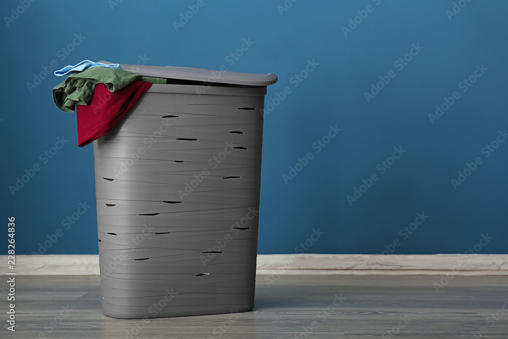 Laundry basket with dirty clothes on floor near color wall