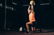 handsome fit sportsman performing lunge with medicine ball overhead in dark gym