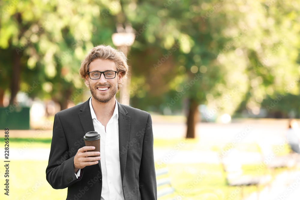 Handsome young businessman with coffee resting in park