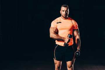 Wall Mural - handsome athletic sportsman working out with barbells in dark gym