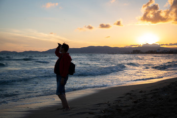 Wall Mural - Older woman looking out to sea and enjoying beautiful sunset on a beach.