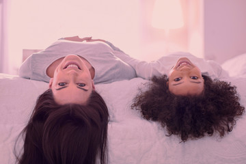 Wall Mural - Upside down. Nice happy mother and daughter looking at you while lying together on the bed