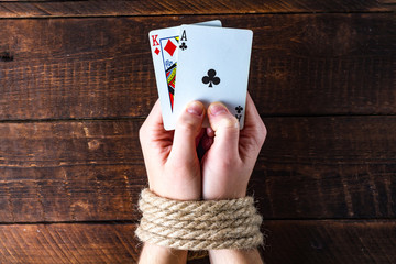 Card addiction. Dependence on poker, gambling. A person with tied hands holding playing cards on a wooden background. Gambling concept