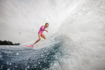 Wall Mural - Young blonde woman wakesurfer riding down the blue splashing wave