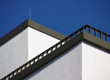 Corner Of A White Building With Diagonal Balcony Railing And Blue Sky