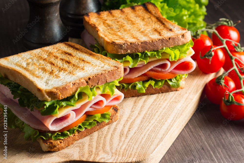 Close-up of two sandwiches with bacon, salami, prosciutto and fresh vegetables on rustic wooden cutting board. Club sandwich concept. - obrazy, fototapety, plakaty 