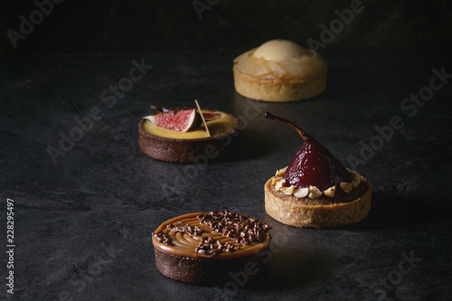 Fotografía Variety of sweet tartlets with chocolate, caramel, pears, figs on black texture table