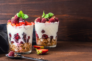 yogurt with muesli and berries in two glasses on dark wooden table